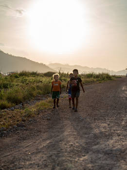 Three kids walking along a dusty dirt road
