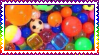 A stamp with a rainbow border depicting a photograph of small multicolored bouncy balls, beads, and cubes.