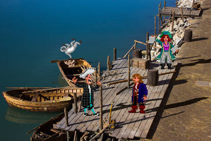 A photo of a small wharf with a couple of rowboats at Parque del Mar, Majorca, with sprites of Stan, Kate Capsize, and Guybrush from LeChuck's Revenge edited into it. To add to the illusion that they are really there, they are casting shadows on the ground. Stan is talking to Guybrush and probably trying to sell him a boat. Kate is standing off to the side, promoting her charter tours. A grey monkey from the game intro is cavorting on one of the boats.