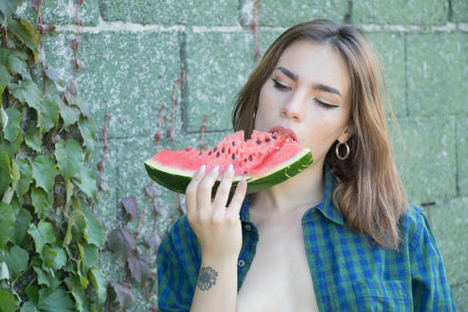 Miriam eating a watermelon near a wall with ivy 01
