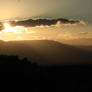Sun behind a cloud about to set below the montain