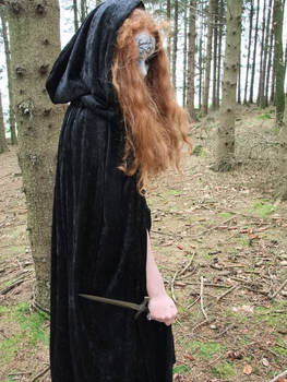 Witch in black coat dagger looking down Stock